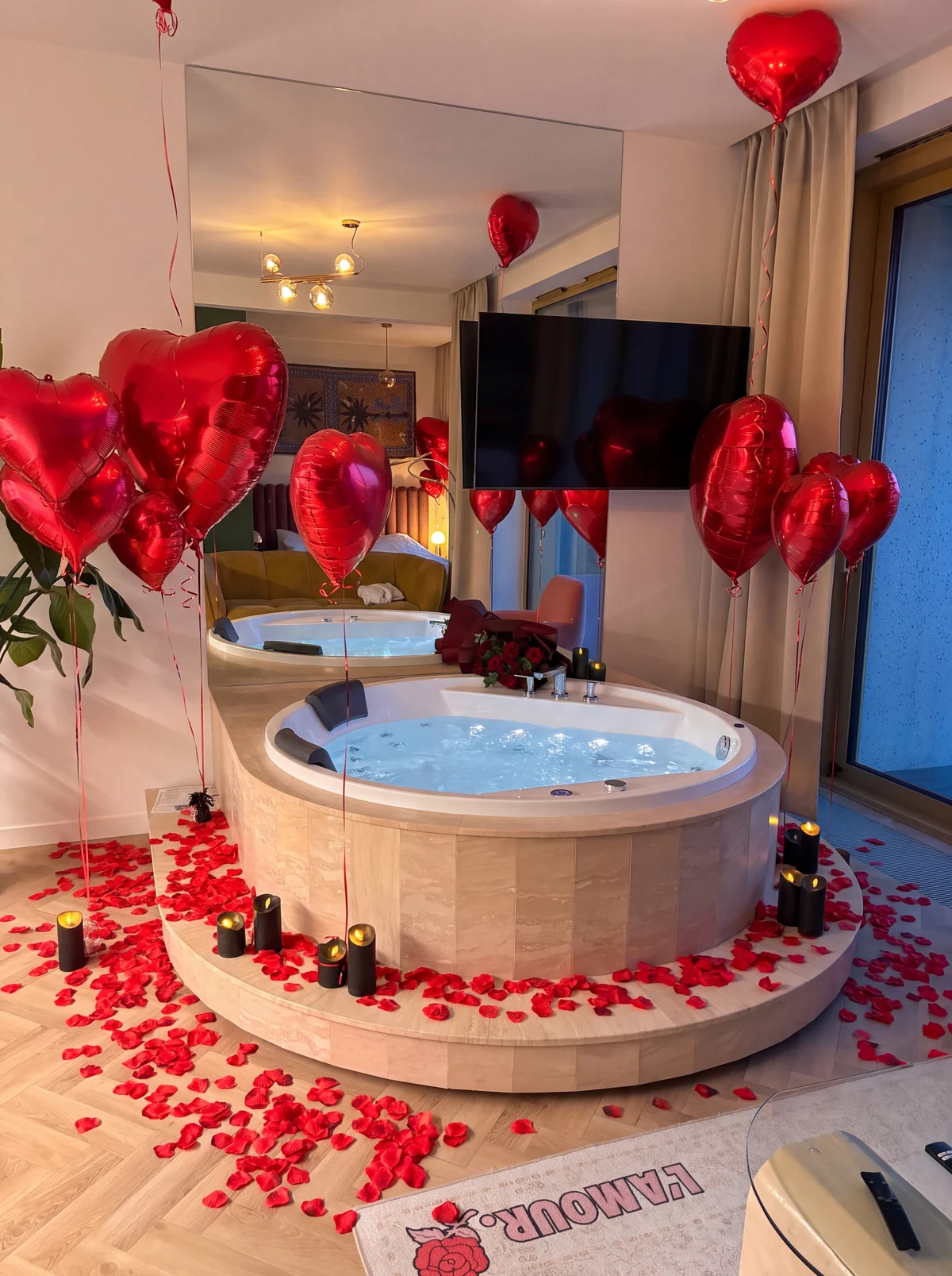 Okrągłe jacuzzi z płatkami róż, balonami i bukietem w apartamencie Boulevard